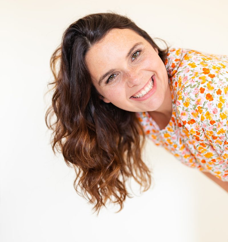 AmberRistow-OurHiddenHive a brunette with curled hair leaning over with a beautiful smile on her face